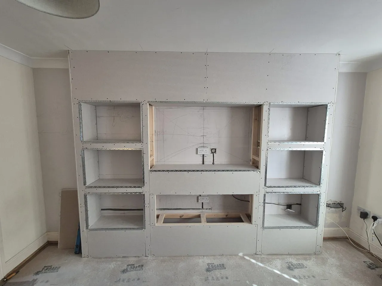 Media wall boarded out with recesses formed for shelving and a fire